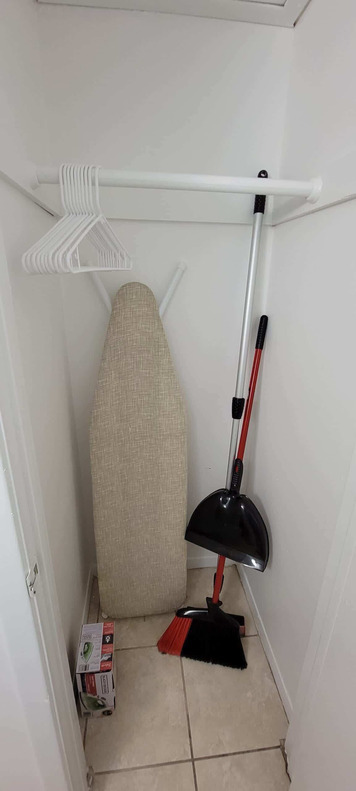 Une petite pièce avec un radiateur blanc, une planche à repasser beige, un balai et une boîte de produits de nettoyage.