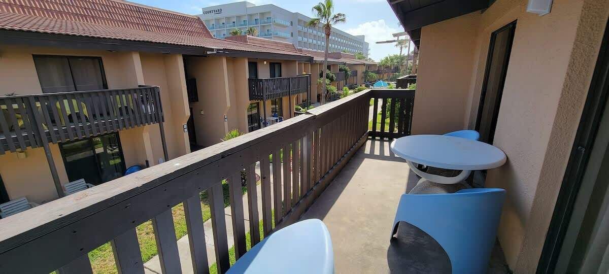 A balcony with a wooden railing, two white tables, and a view of adjacent buildings.