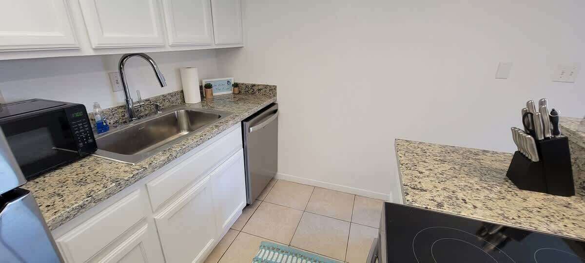 A compact kitchen with white cabinets, a stainless steel sink, a microwave, and a dishwasher.