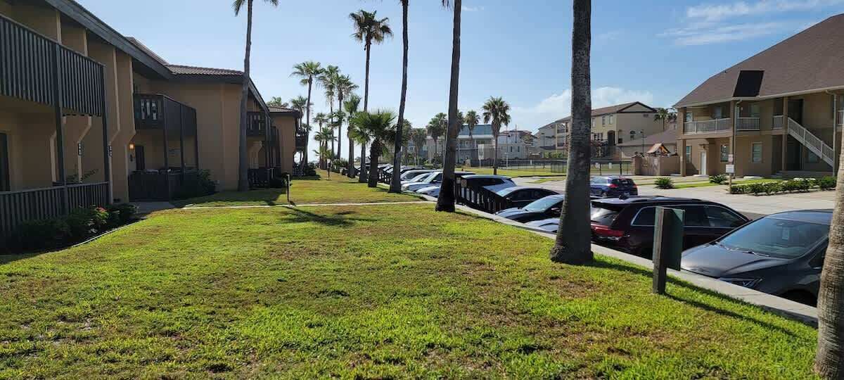 Een parkeerplaats met verschillende auto's, een gazon en gebouwen met balkons en palmbomen.
