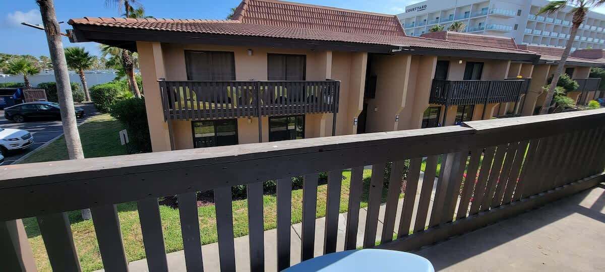 Un hotel con balcón, aparcamiento y un edificio con tejado de tejas.