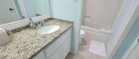Un baño con lavamanos de encimera de granito, un espejo, inodoro y zona de ducha.