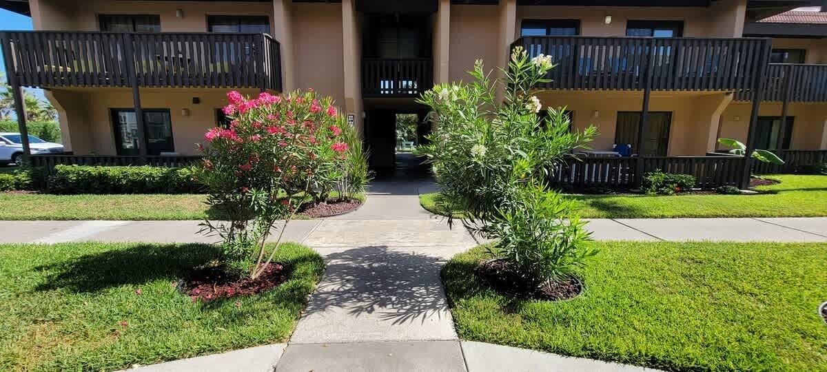 A building with a central entrance, surrounded by well-maintained lawns and flowering plants.