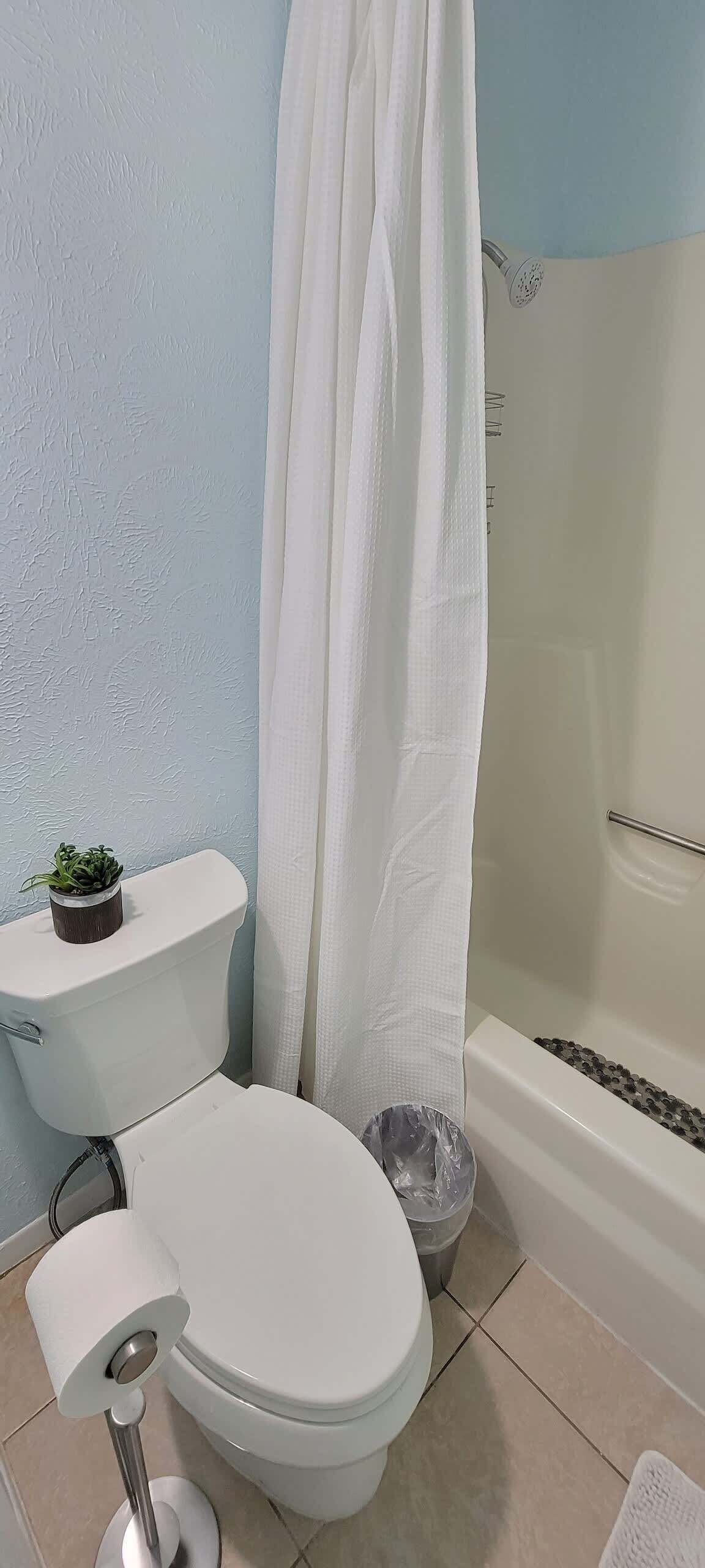 A bathroom with a toilet, a shower curtain, a bathtub, and a small potted plant on the toilet tank.