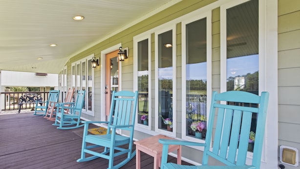 A covered porch with rocking chairs and a table, large windows with curtains, and a view of the outdoors. - Beautifully Renovated Waterfront House in Gulfport (Gulfport)
