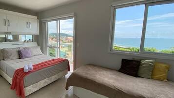 A bedroom with a bed, a sofa, a window with a view of the sea, and a kitchenette.