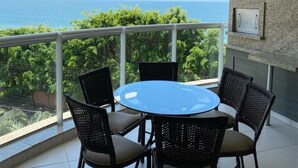 A balcony with a round table and four chairs, overlooking a scenic view of the ocean and greenery. - Nautilus Premium View - Penha - SC (Penha)