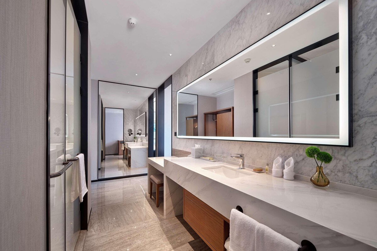 Une salle de bain moderne avec un grand miroir, des plans de travail en marbre et une cabine de douche en verre.