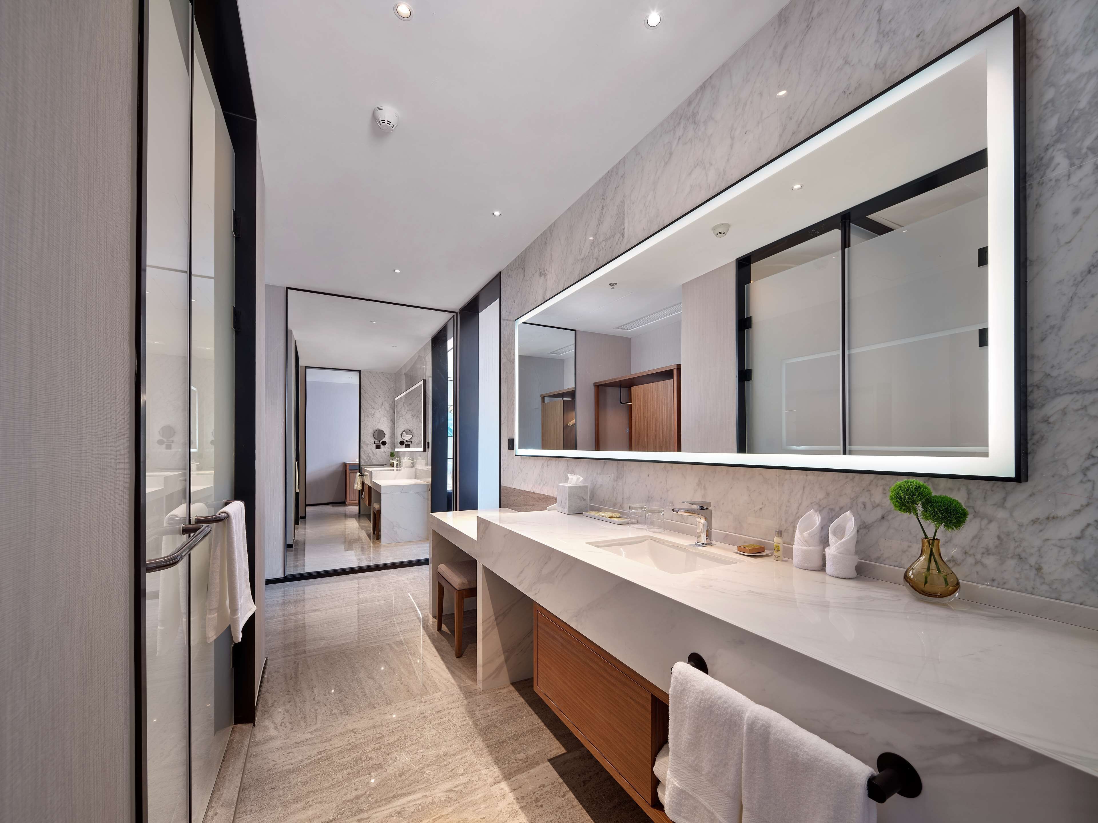 A modern bathroom with a large mirror, marble countertops, and a wooden vanity.