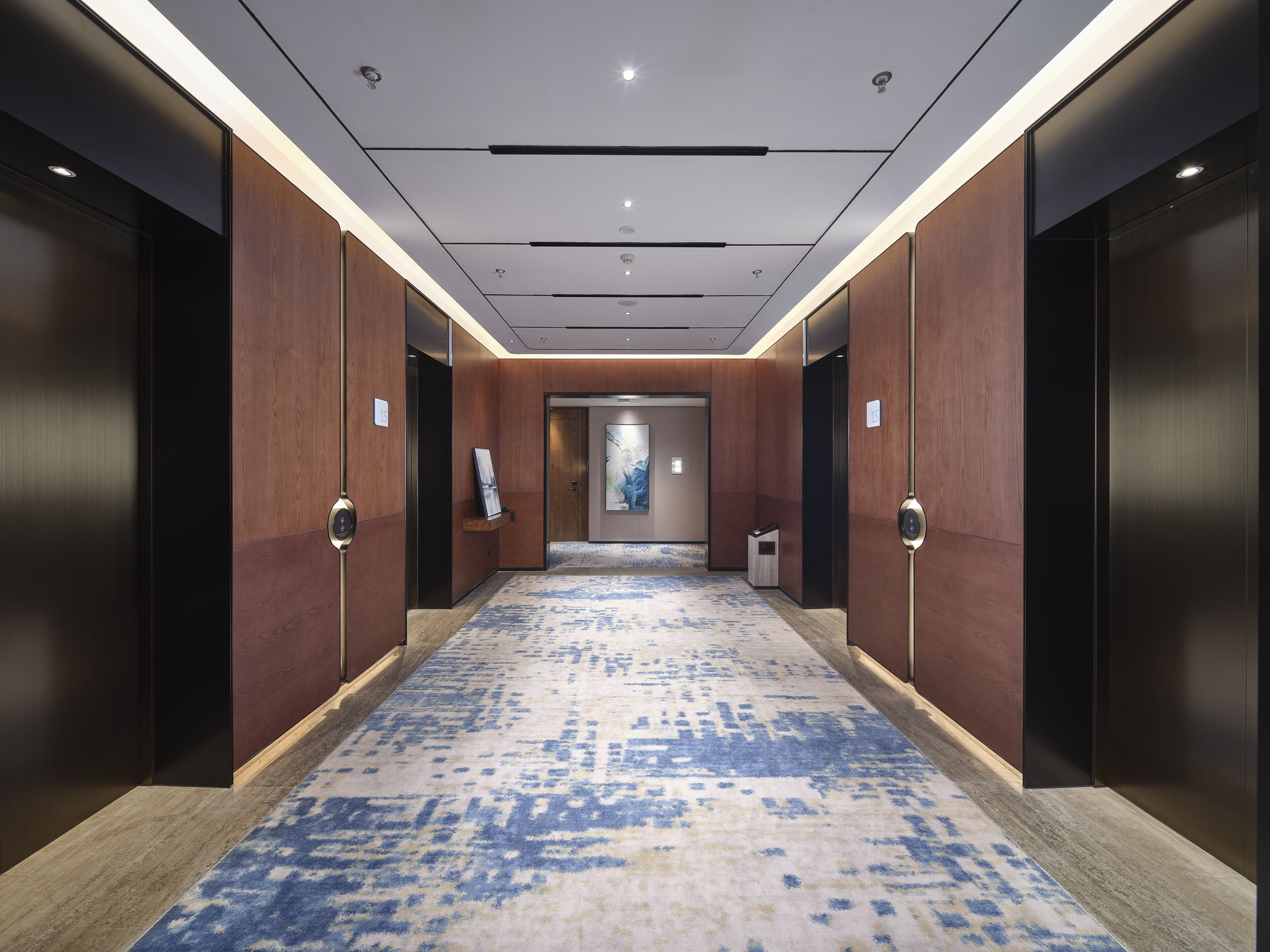 A modern hotel corridor with wooden panel walls, a patterned carpet, and recessed lighting.