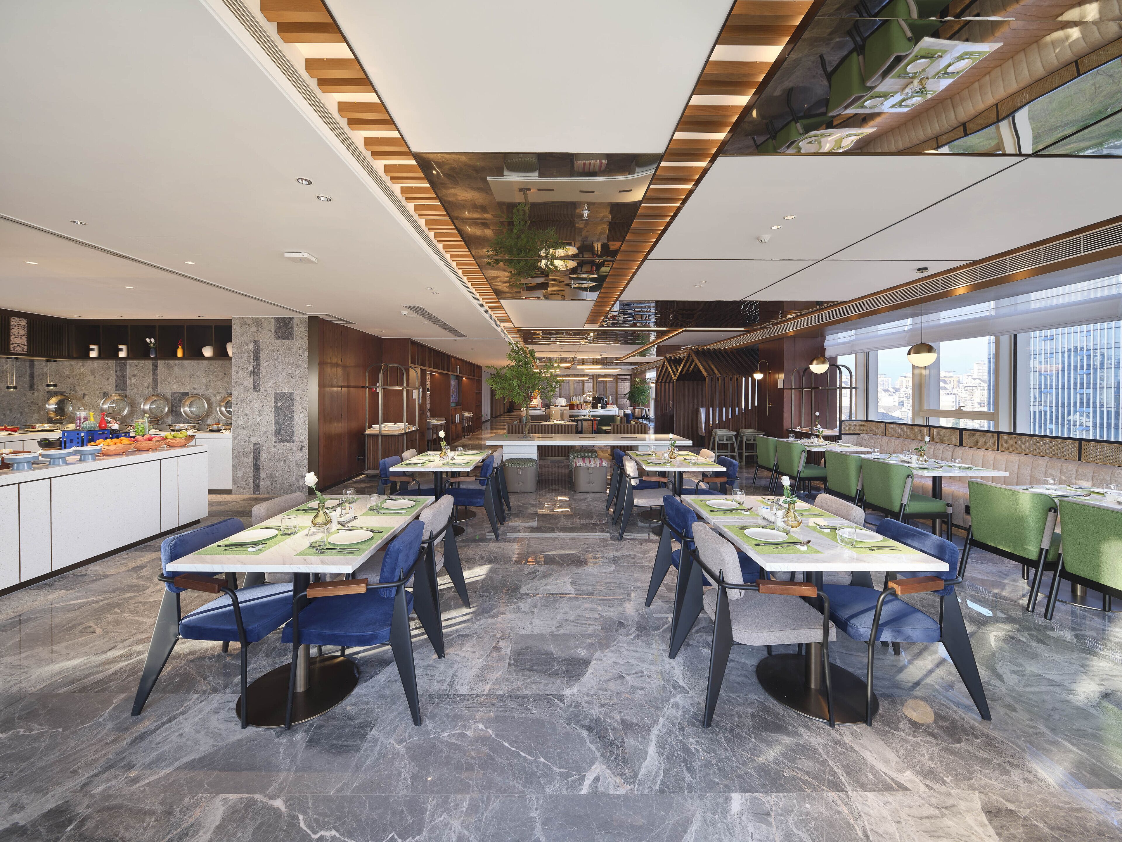 A modern restaurant with marble floors, green and blue chairs, and a central island with food displays.