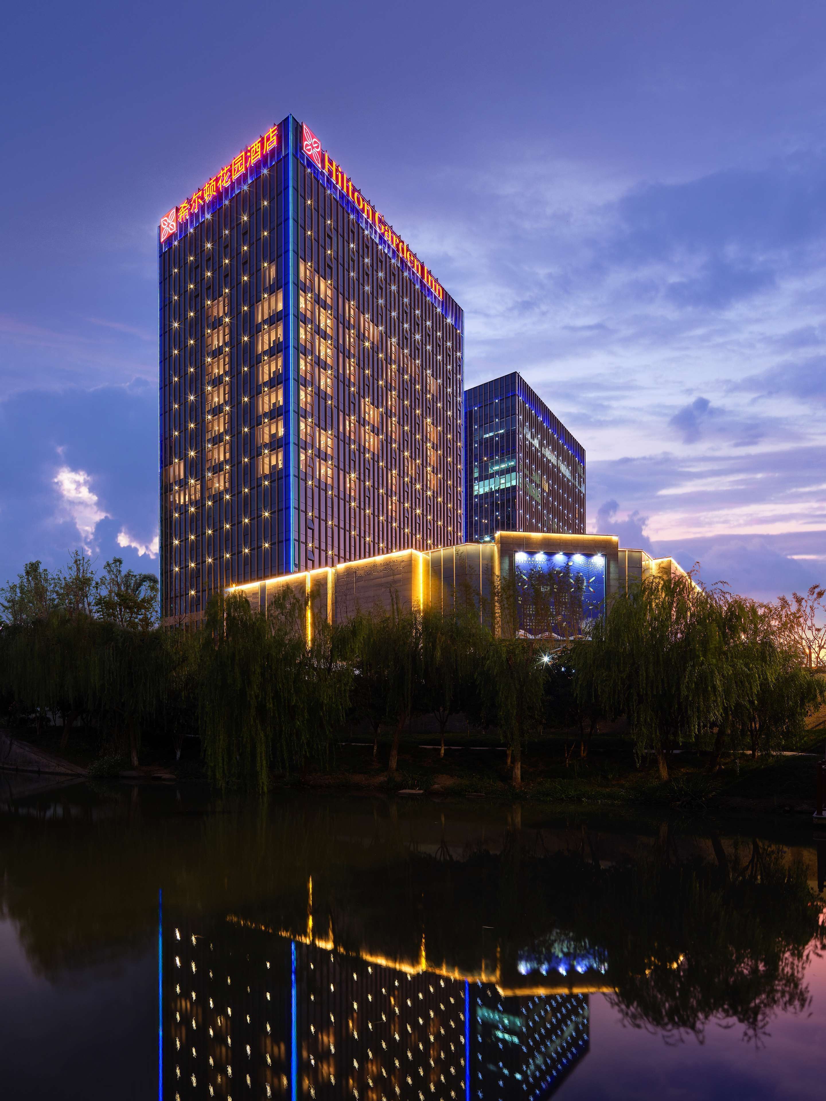 Ein modernes Hotel mit einem spiegelnden Pool davor, mit einem markanten Gebäude und beleuchteter Beschilderung.