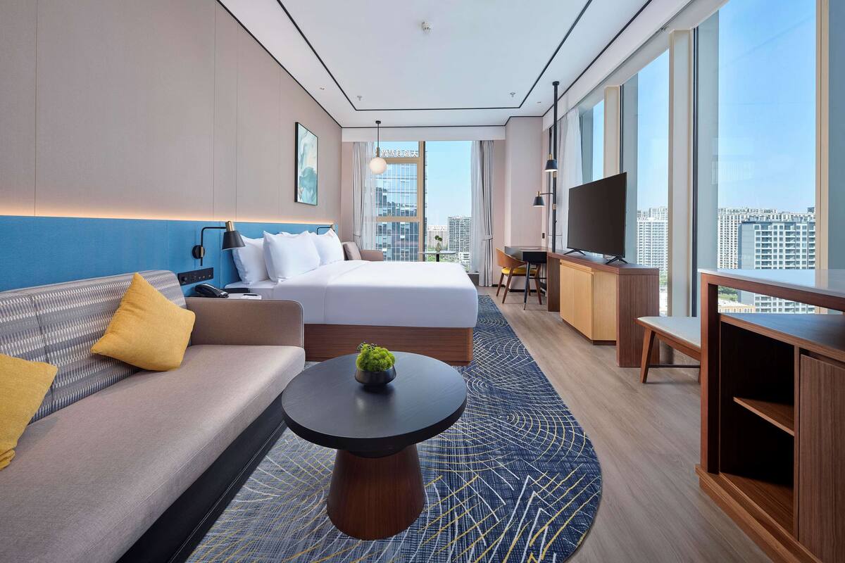 Ein modernes Hotelzimmer mit einem großen Bett, einer Couch, einem Schreibtisch und einem Fernseher.