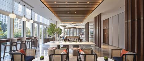 A spacious lobby with modern furnishings, large windows, and a central seating area.