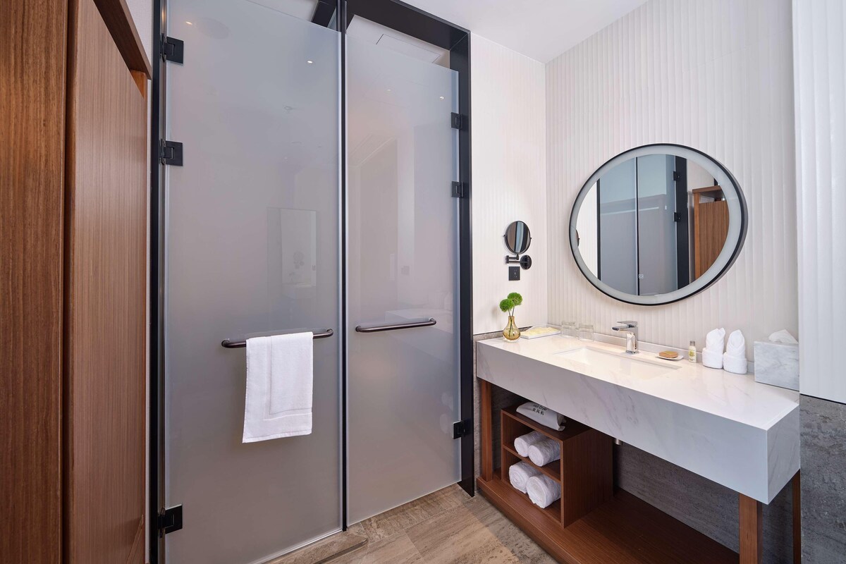 Een moderne badkamer met een dubbele deur, een ronde spiegel, een wastafel met een marmeren blad en een handdoekhouder.