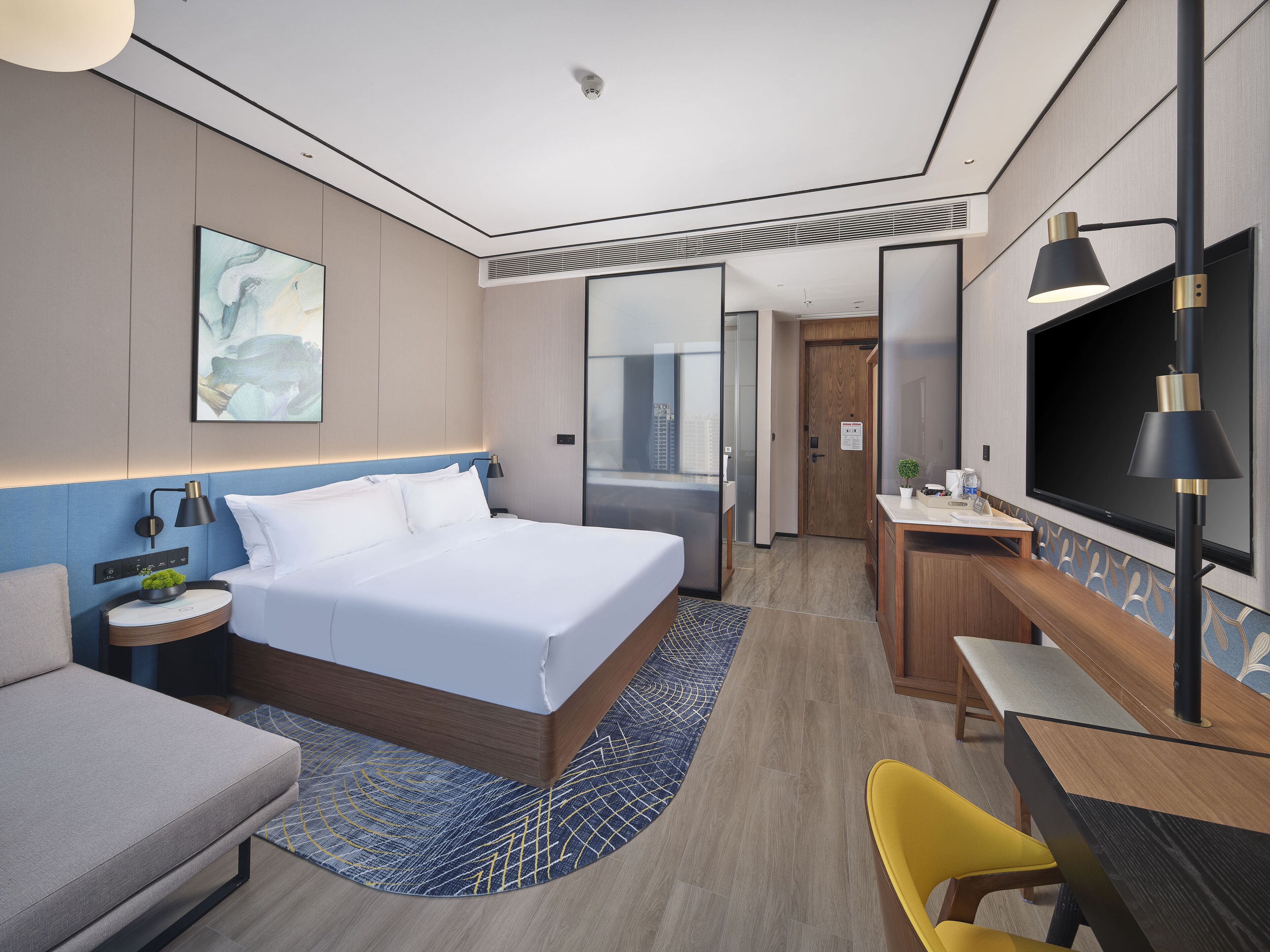 Habitación de hotel moderna con una cama grande, un escritorio, una silla, un televisor y una ventana con vistas a edificios.