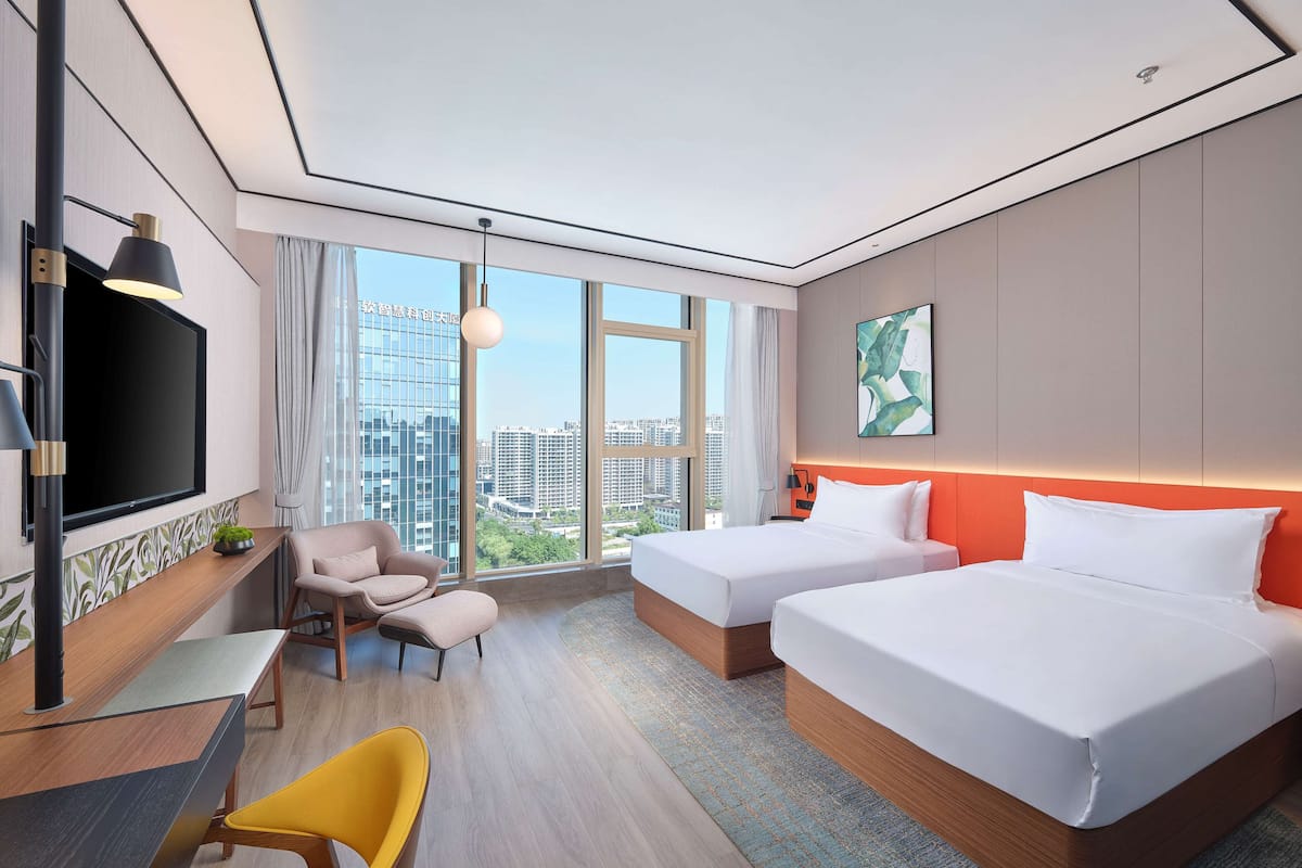 Ein modernes Hotelzimmer mit zwei Betten, einem Fernseher, einem Schreibtisch und Blick auf die Stadt.