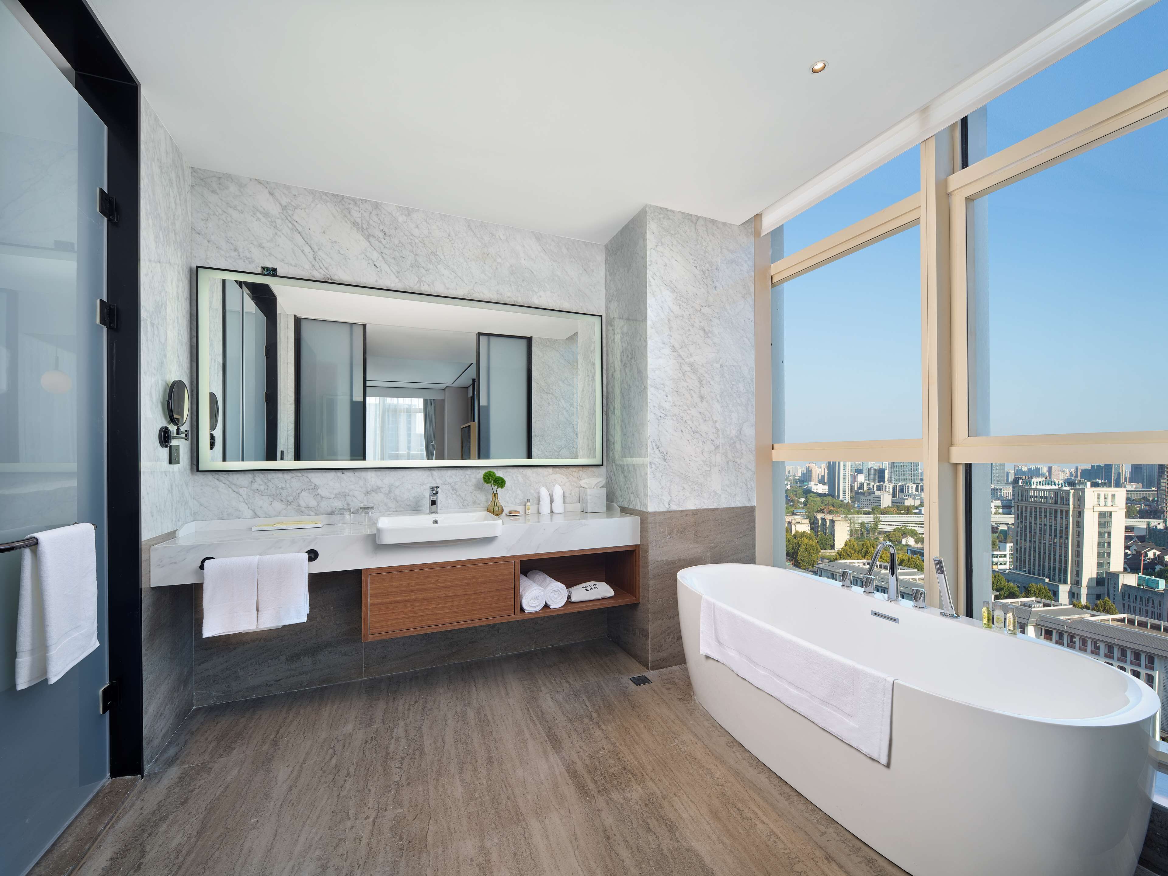 Un baño moderno con un espejo grande, una bañera y vistas a la ciudad.