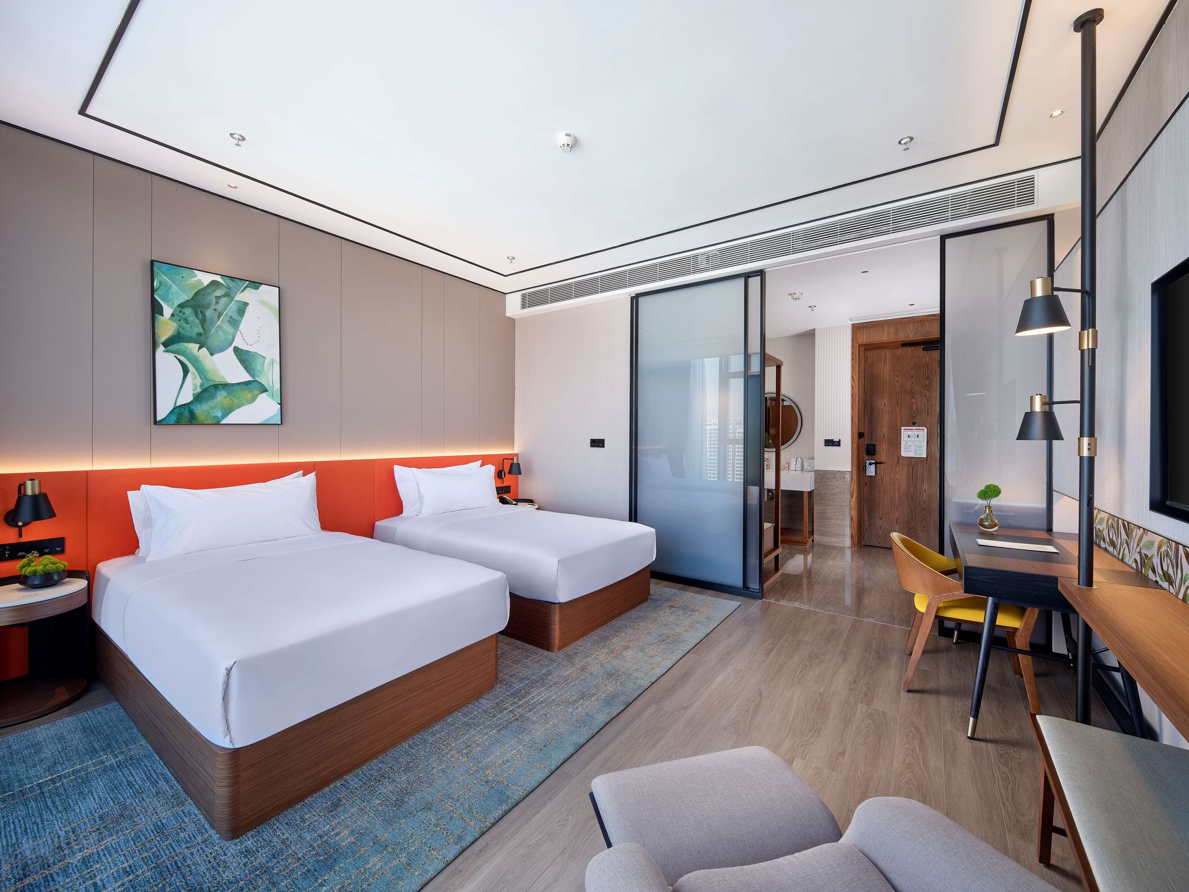 A modern hotel room with two beds, a desk, a chair, and a large mirror.