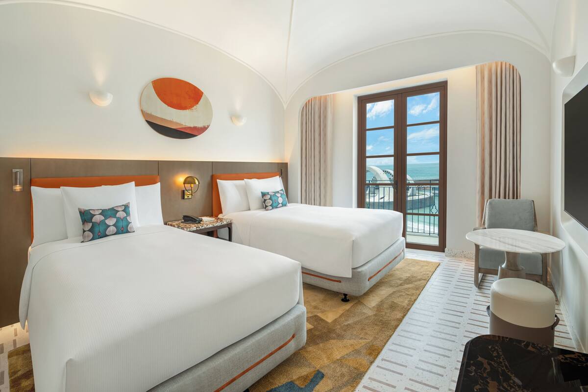 A hotel room with two beds, a desk, a chair, and a TV.