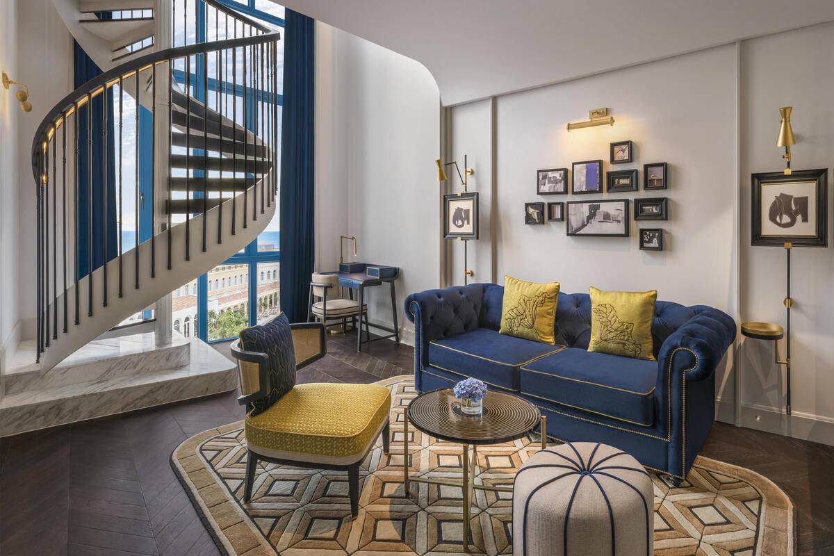 A modern living room with a blue sofa, yellow cushions, a round coffee table, and a spiral staircase.