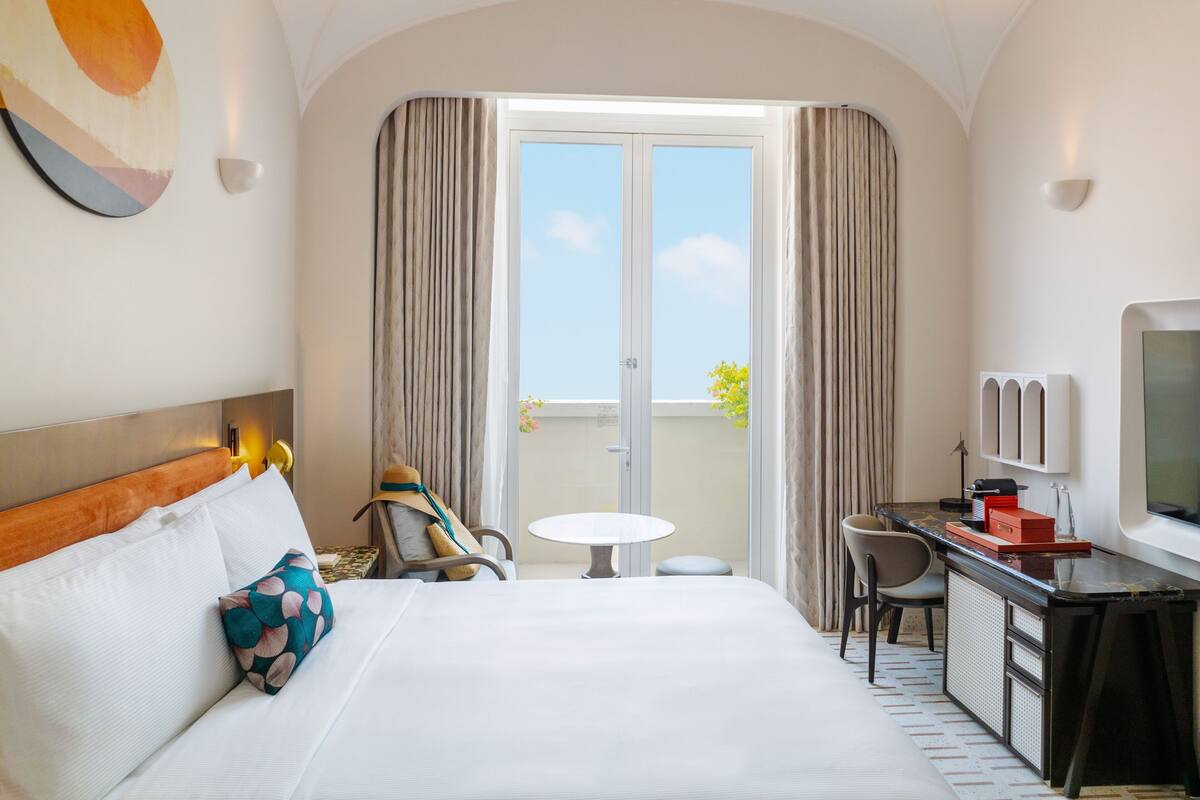 A hotel room with a bed, a desk, a chair, a small table, and a TV.