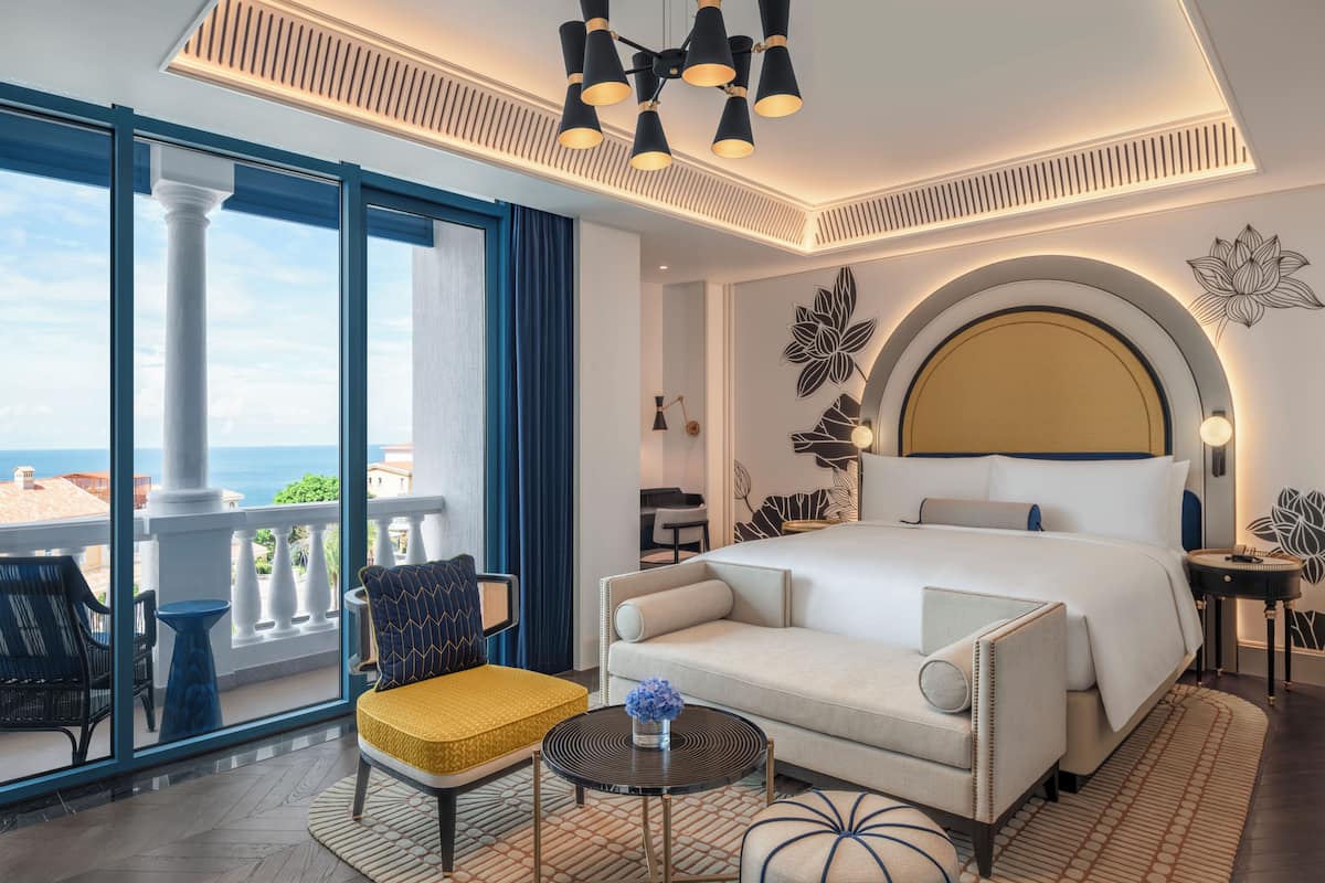 A hotel room with a large bed, a balcony with a view, a round table, and a sofa.