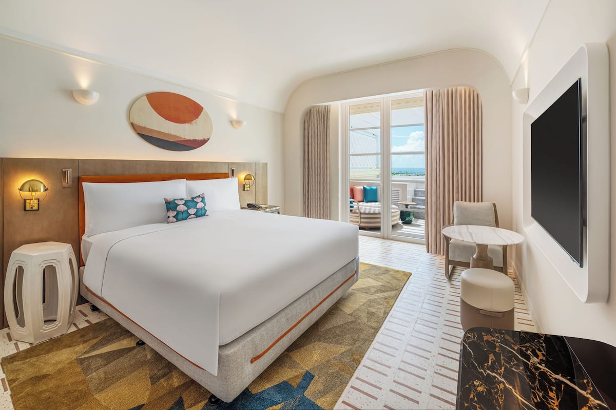 A hotel room with a large bed, a TV, a seating area, and a view of the ocean.