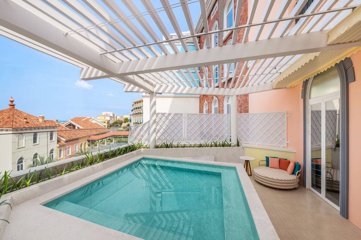 A rooftop pool area with a white pergola, a sofa, and a view of the cityscape.