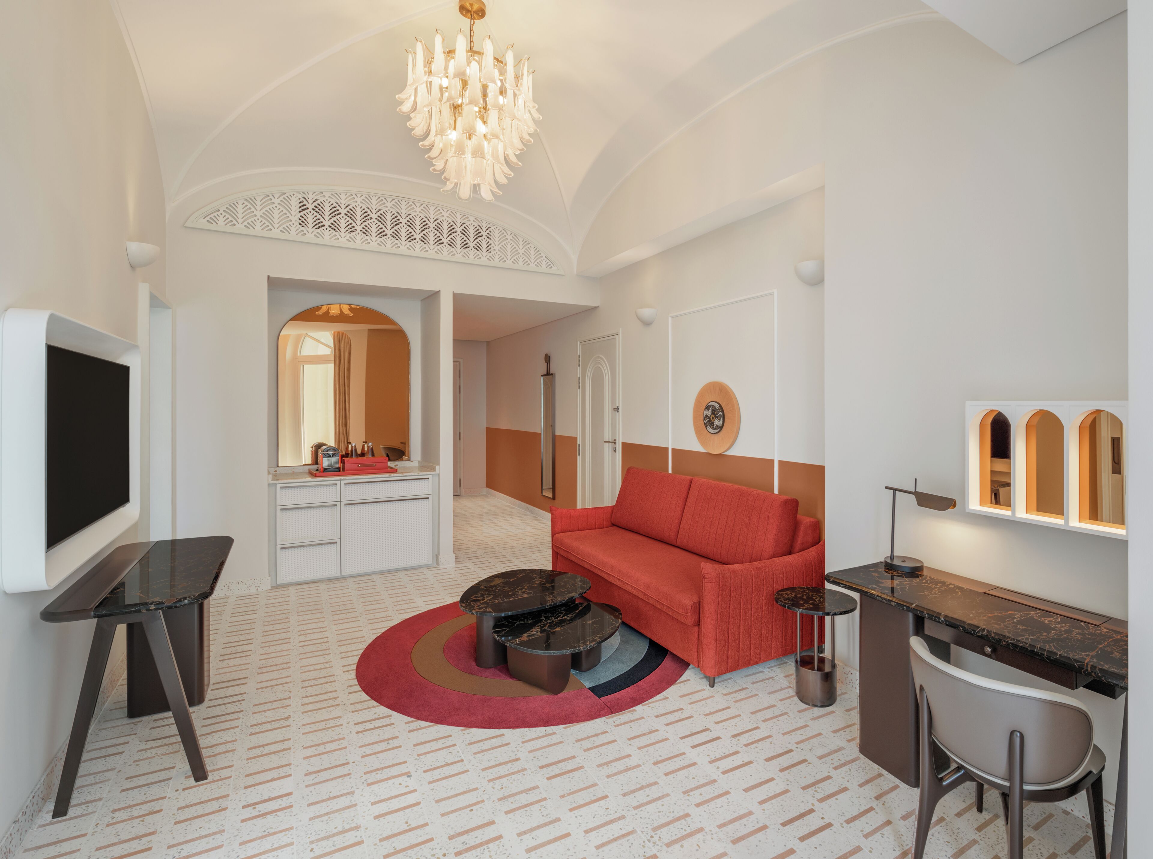A modern living room with a red sofa, a TV, a coffee table, and a chandelier.