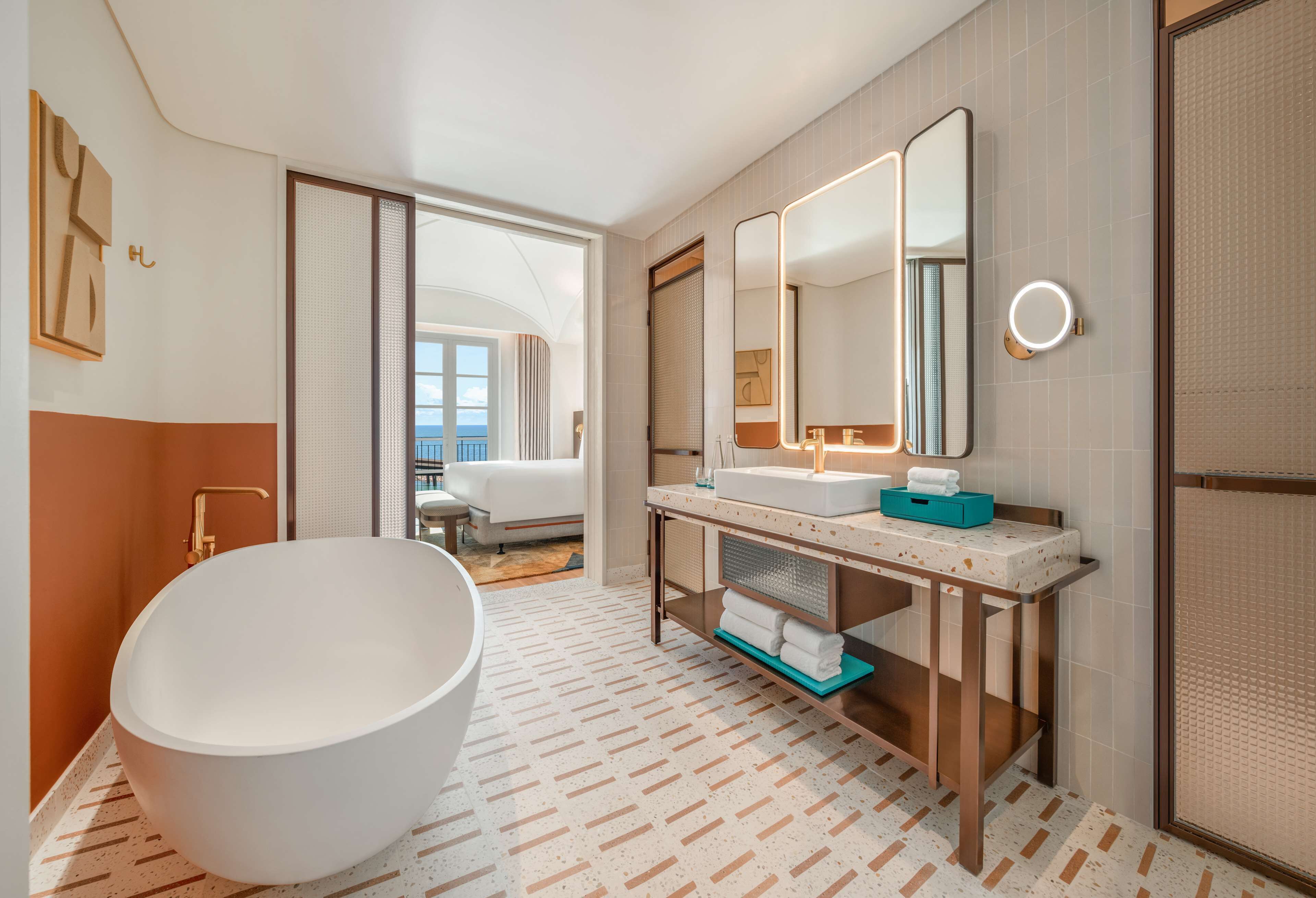 Un baño moderno con una bañera independiente, un tocador con espejo y vistas a un balcón.