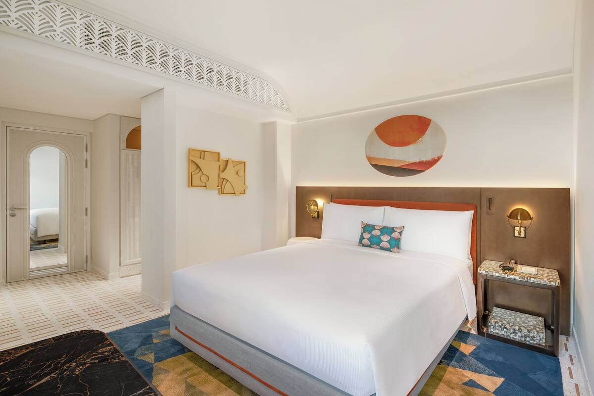 A hotel room with a large bed, a nightstand, a wall-mounted lamp, and a decorative wall piece.