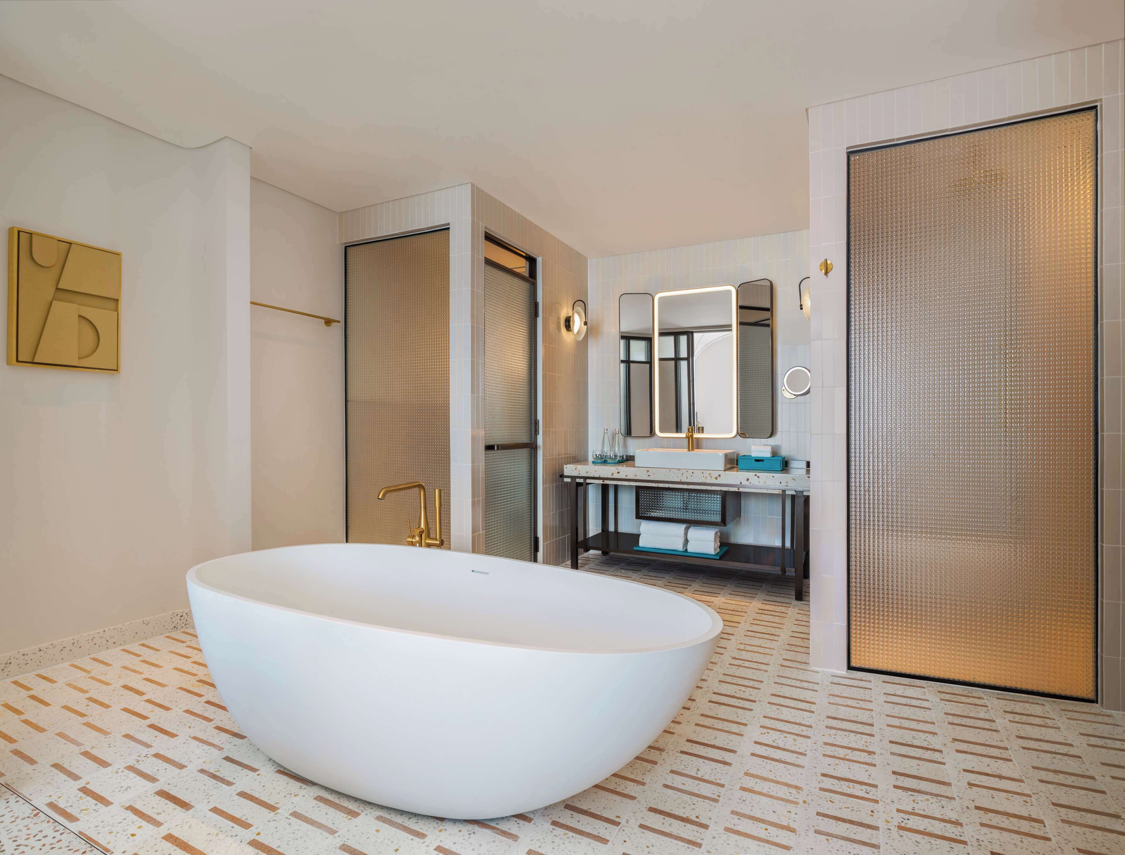 Un baño moderno con una bañera independiente, un espejo grande y un tocador con lavamanos y toallero.