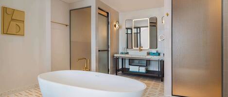 Un baño moderno con una bañera independiente, un espejo grande y un tocador con lavamanos y toallero.