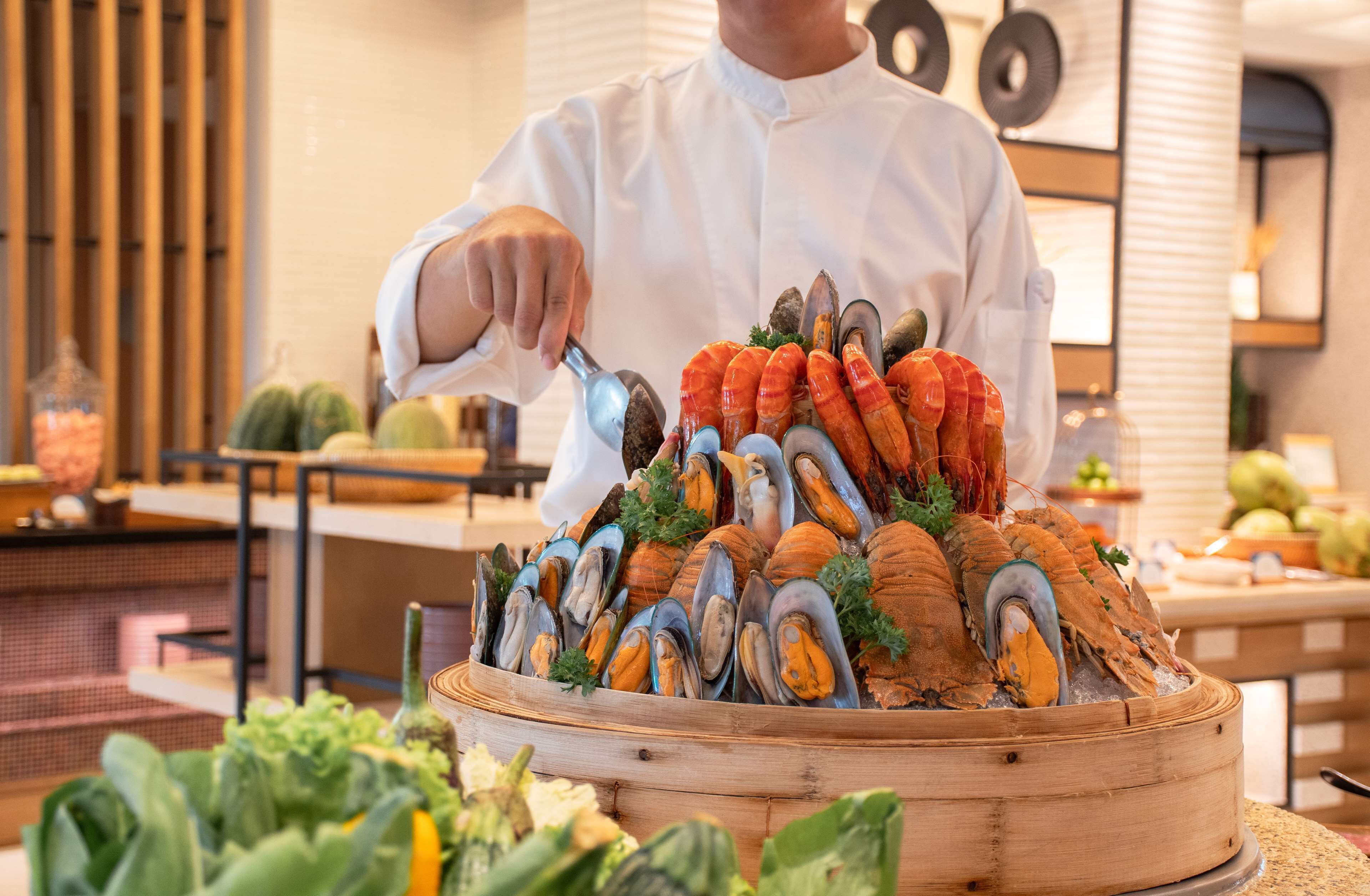 A chef arranging seafood on a wooden platter in a modern kitchen setting.