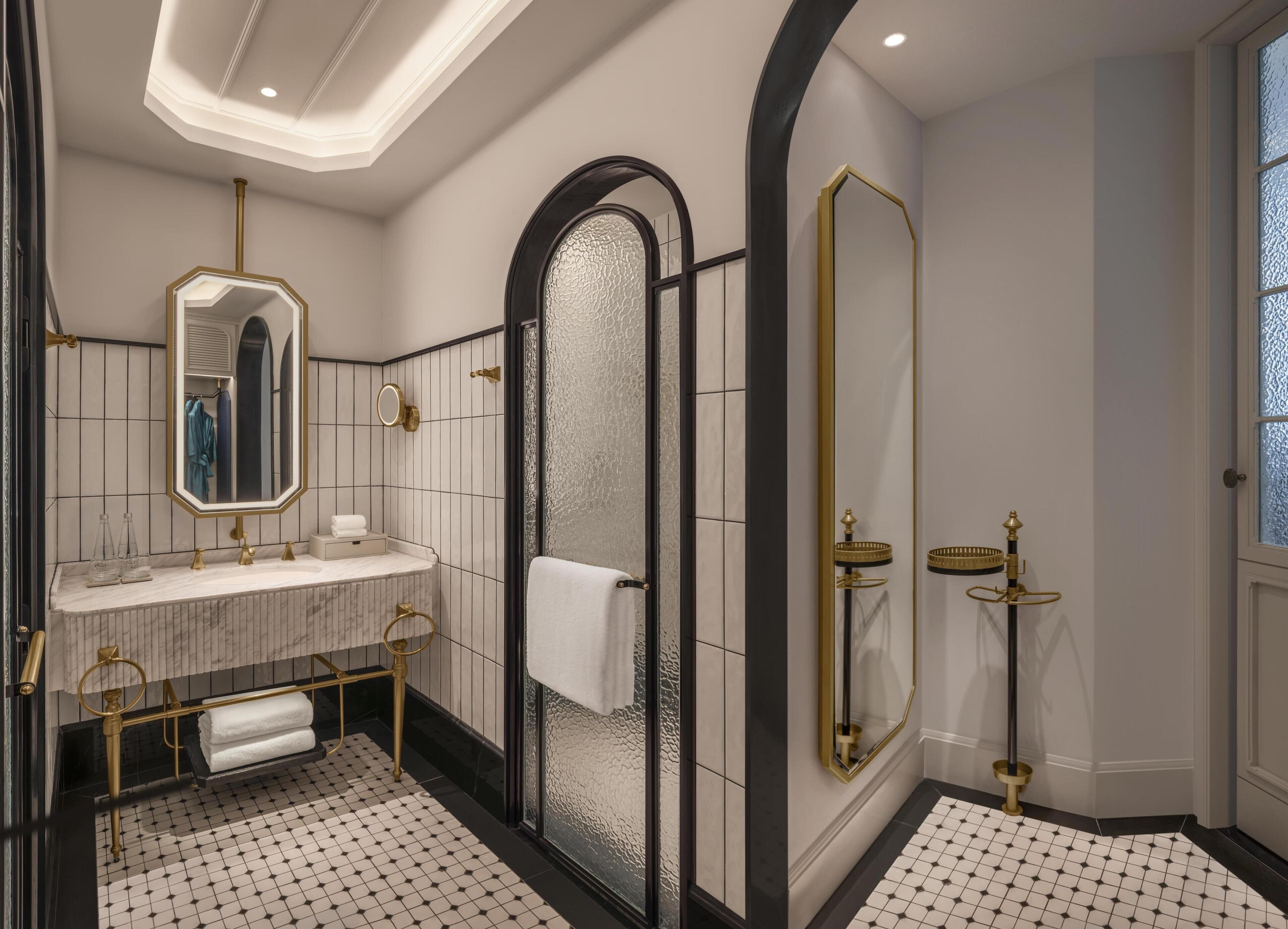 Une salle de bain moderne avec un meuble-lavabo en marbre, un grand miroir, une douche en verre et des accessoires dorés.