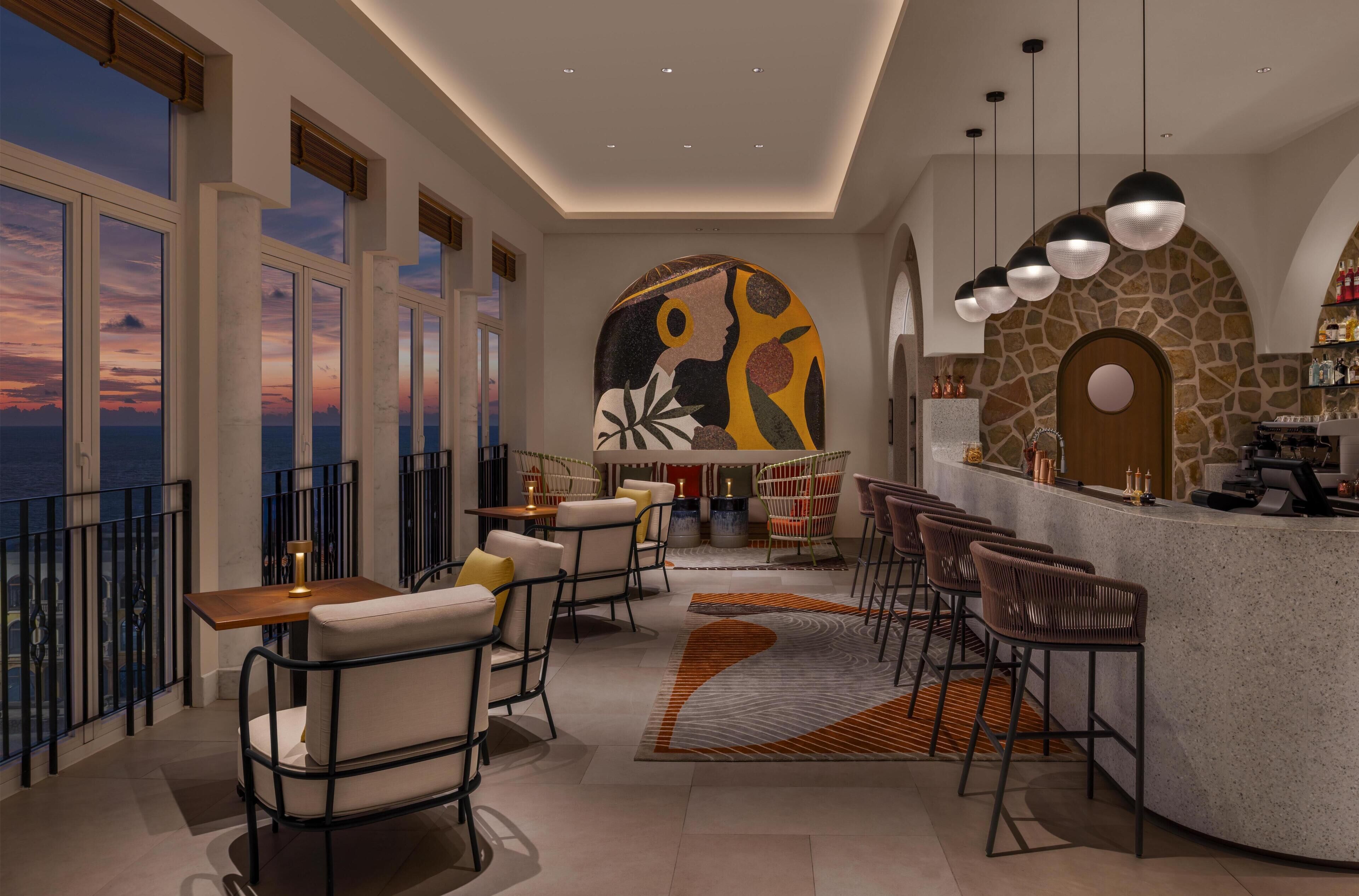 A modern bar area with seating, a stone wall, and a view of the sunset.