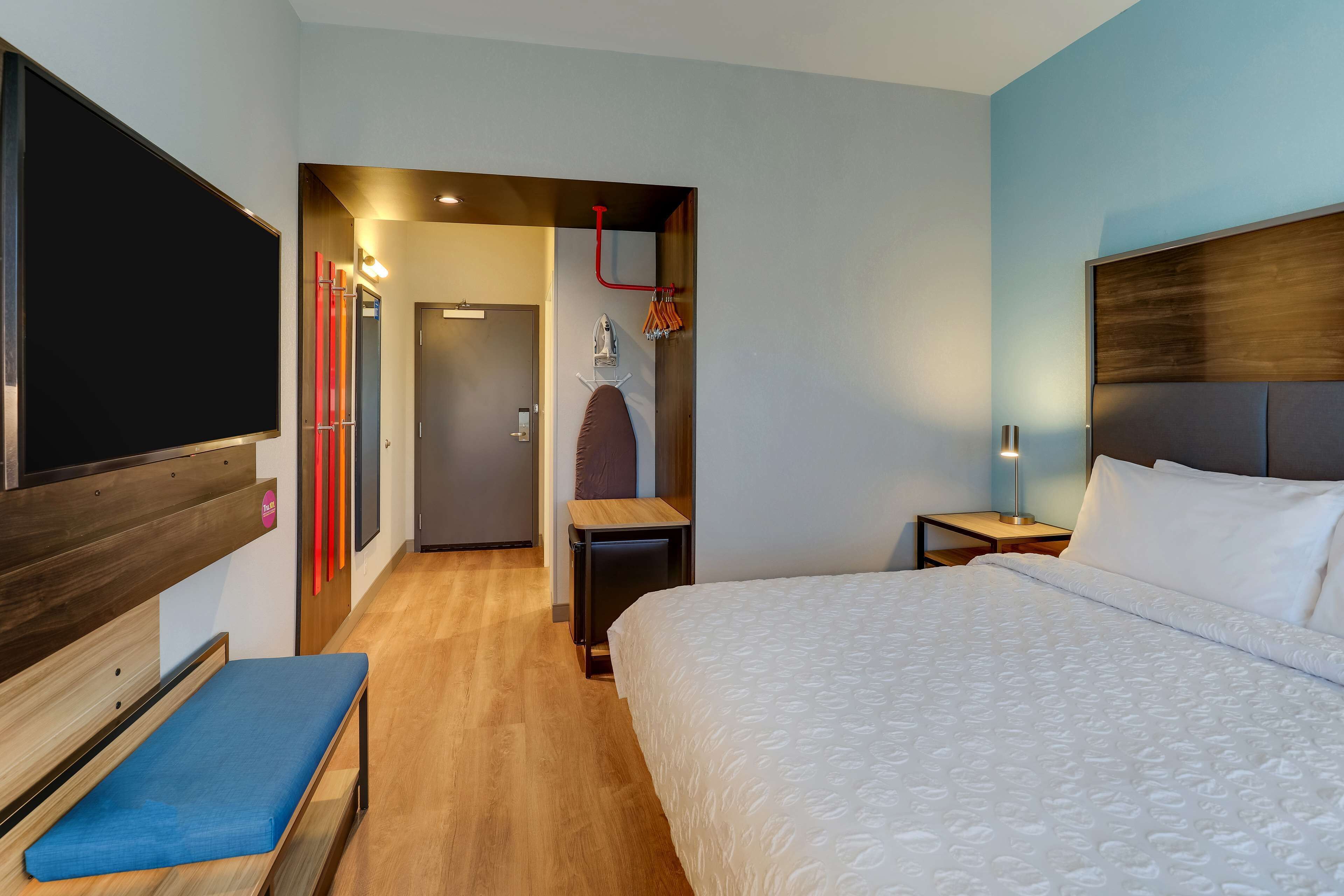 A hotel room with a large bed, a bench, a TV, a desk, and a door leading to a bathroom.