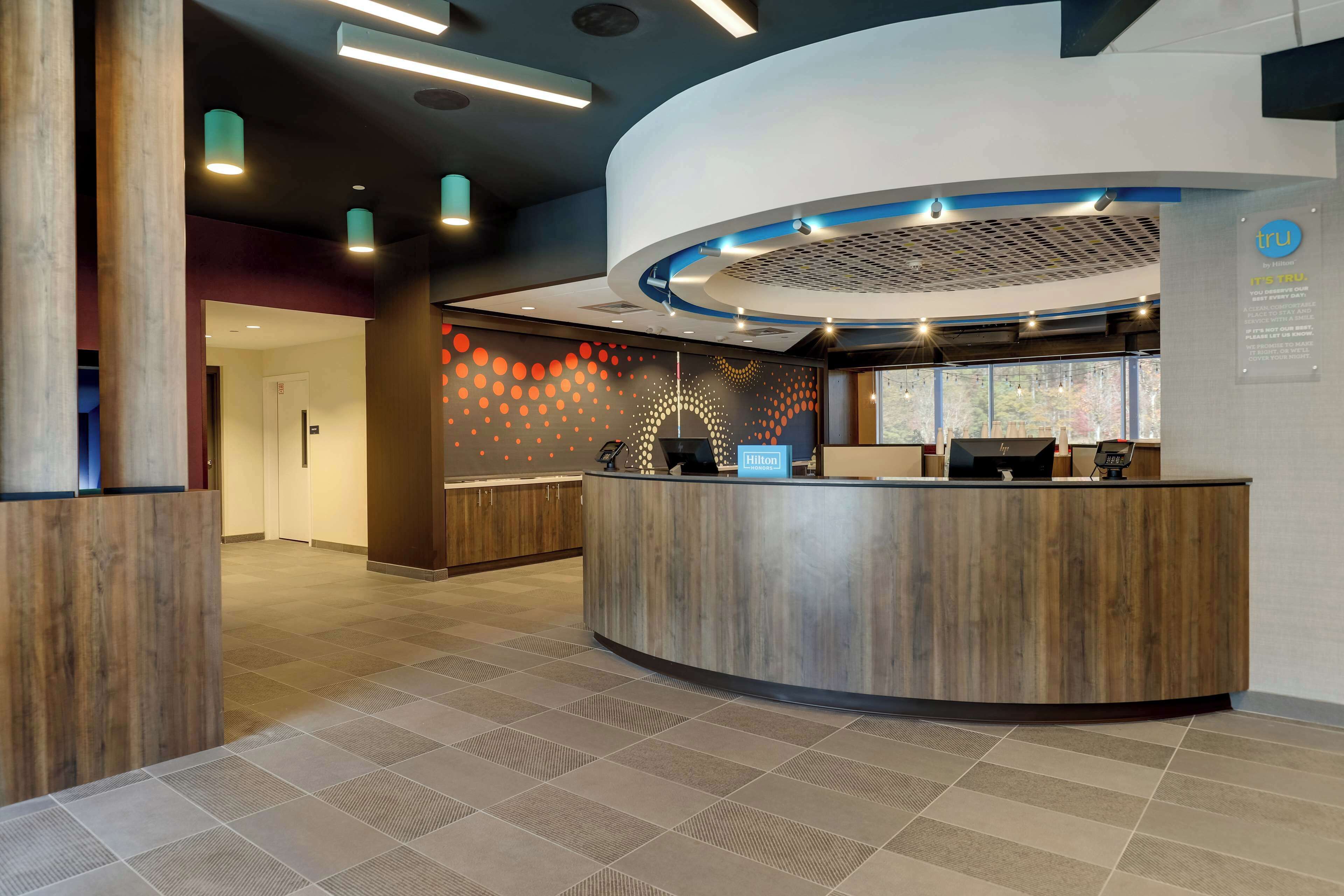 A modern hotel reception area with a curved reception desk, a digital screen, and a sign indicating it's a Hilton hotel.