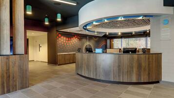 A modern hotel reception area with a curved reception desk, a digital screen, and a sign indicating it's a Hilton hotel.