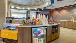 Una estación de bebidas de autoservicio con variedad de bebidas y aperitivos, una sección refrigerada y una pared con diseño circular.