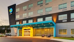 Un hotel moderno con un llamativo letrero 'tru by Hilton', un amplio acceso con toldo azul y un estacionamiento frente a él.