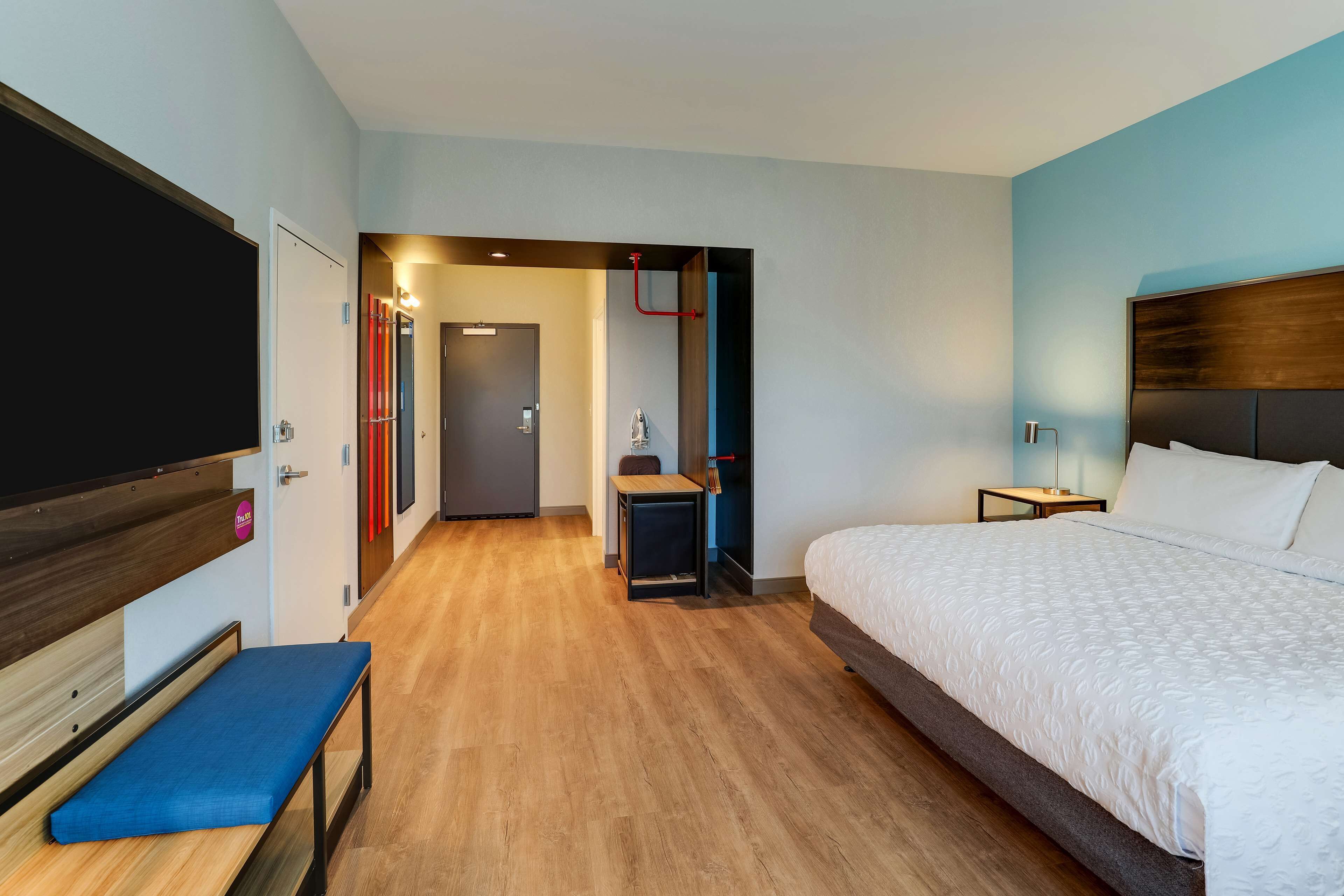 A hotel room with a large bed, a bench, a desk, and a television.