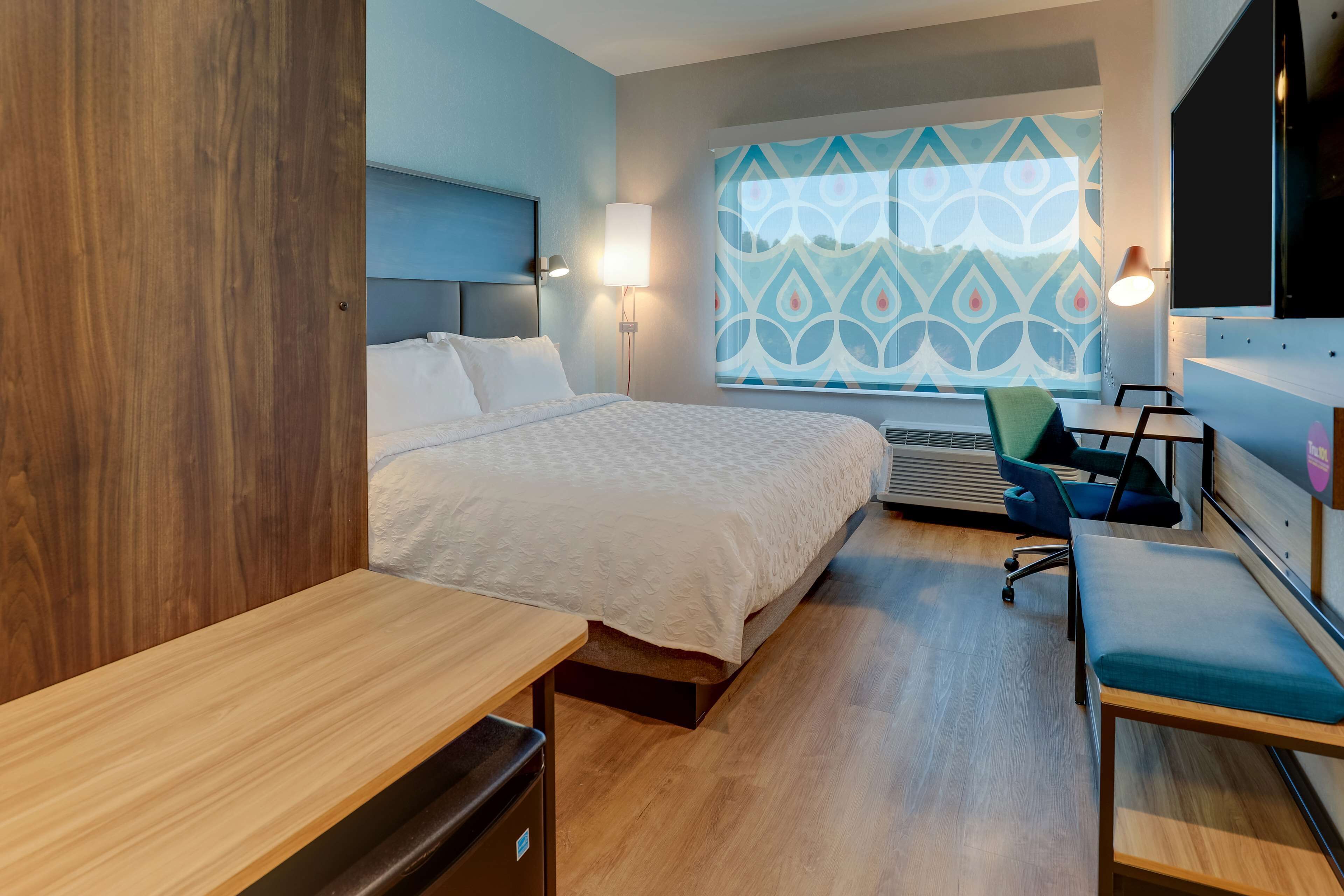 Una habitación de hotel moderna con cama, escritorio, silla y un amplio ventanal con un diseño geométrico.