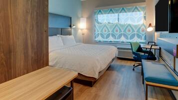 Una habitación de hotel moderna con cama, escritorio, silla y un amplio ventanal con un diseño geométrico.
