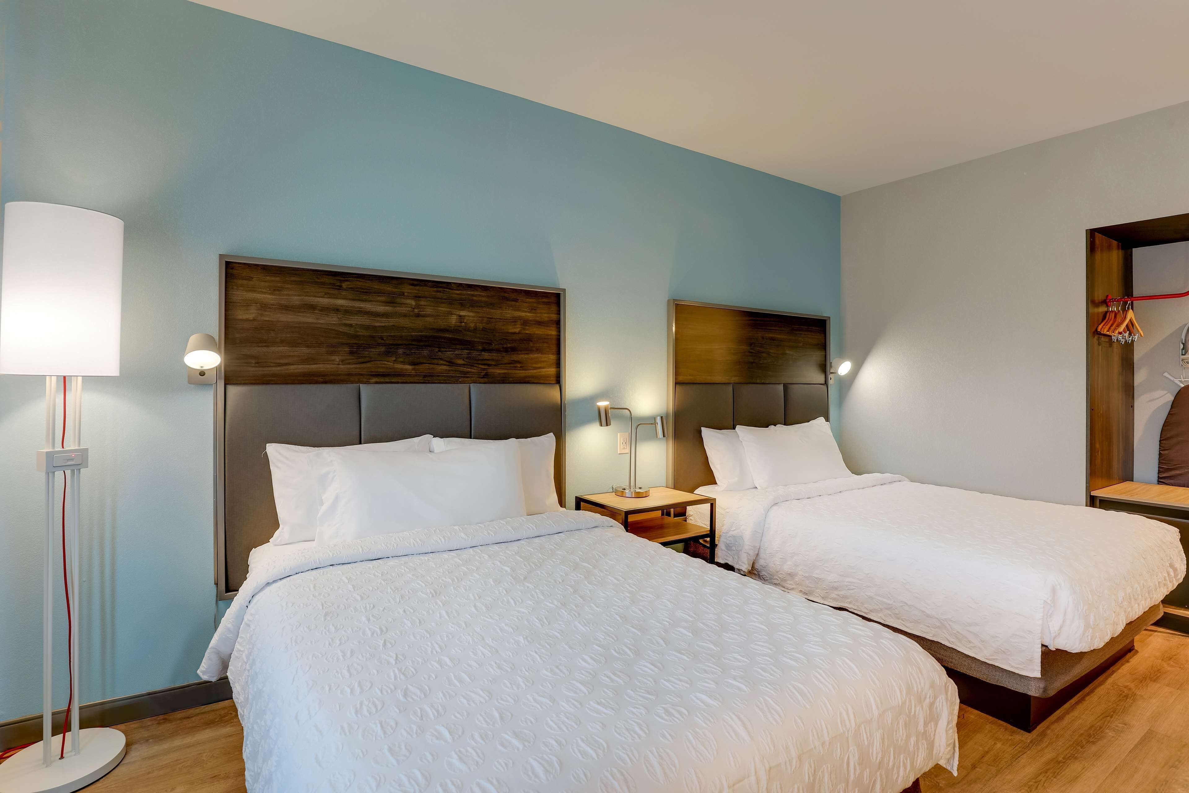 Een hotelkamer met twee bedden, een nachtkastje met een lamp en een wandplank.
