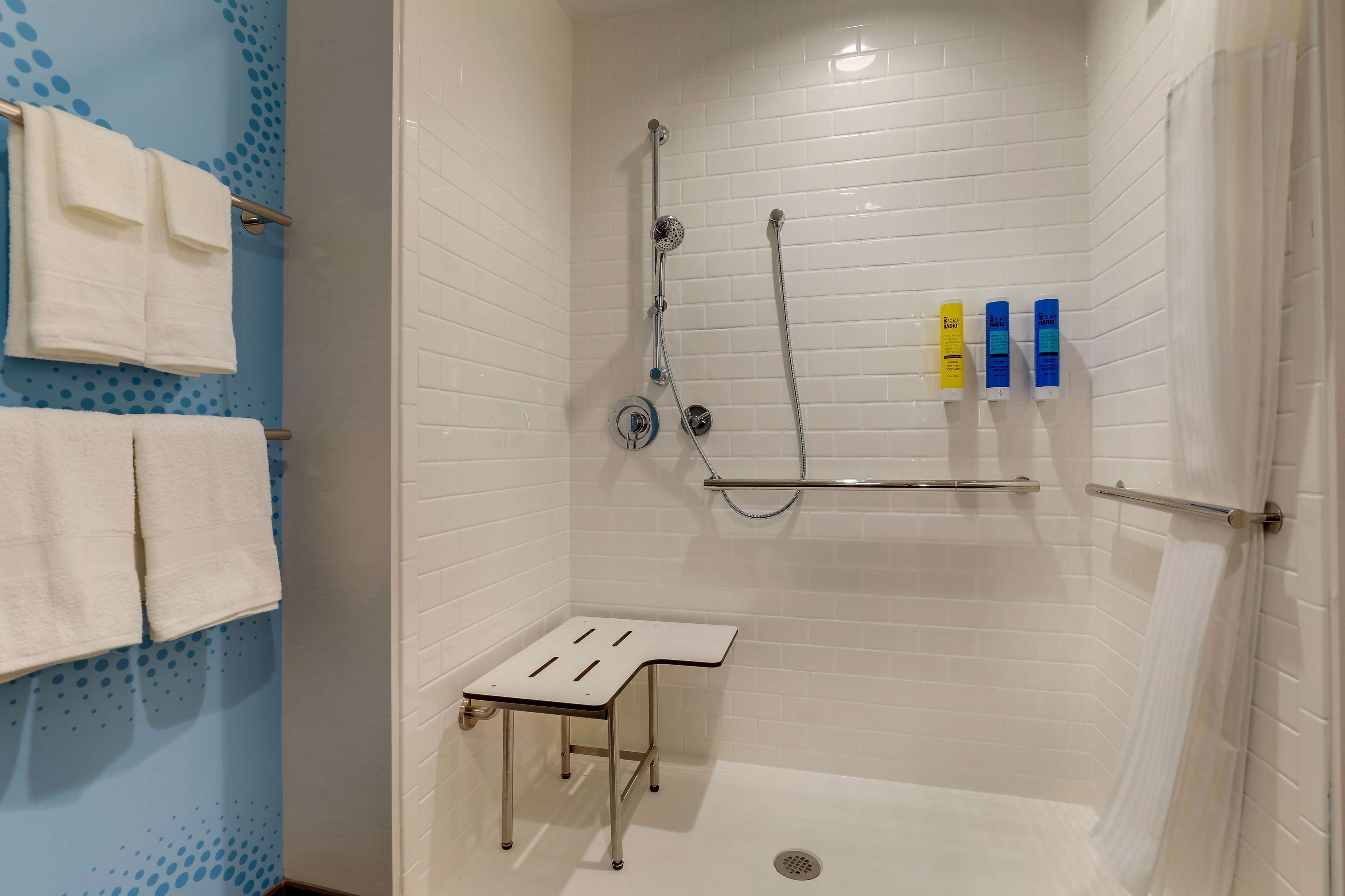 A shower area with white tiled walls, a white shower seat, and a shelf with toiletries.