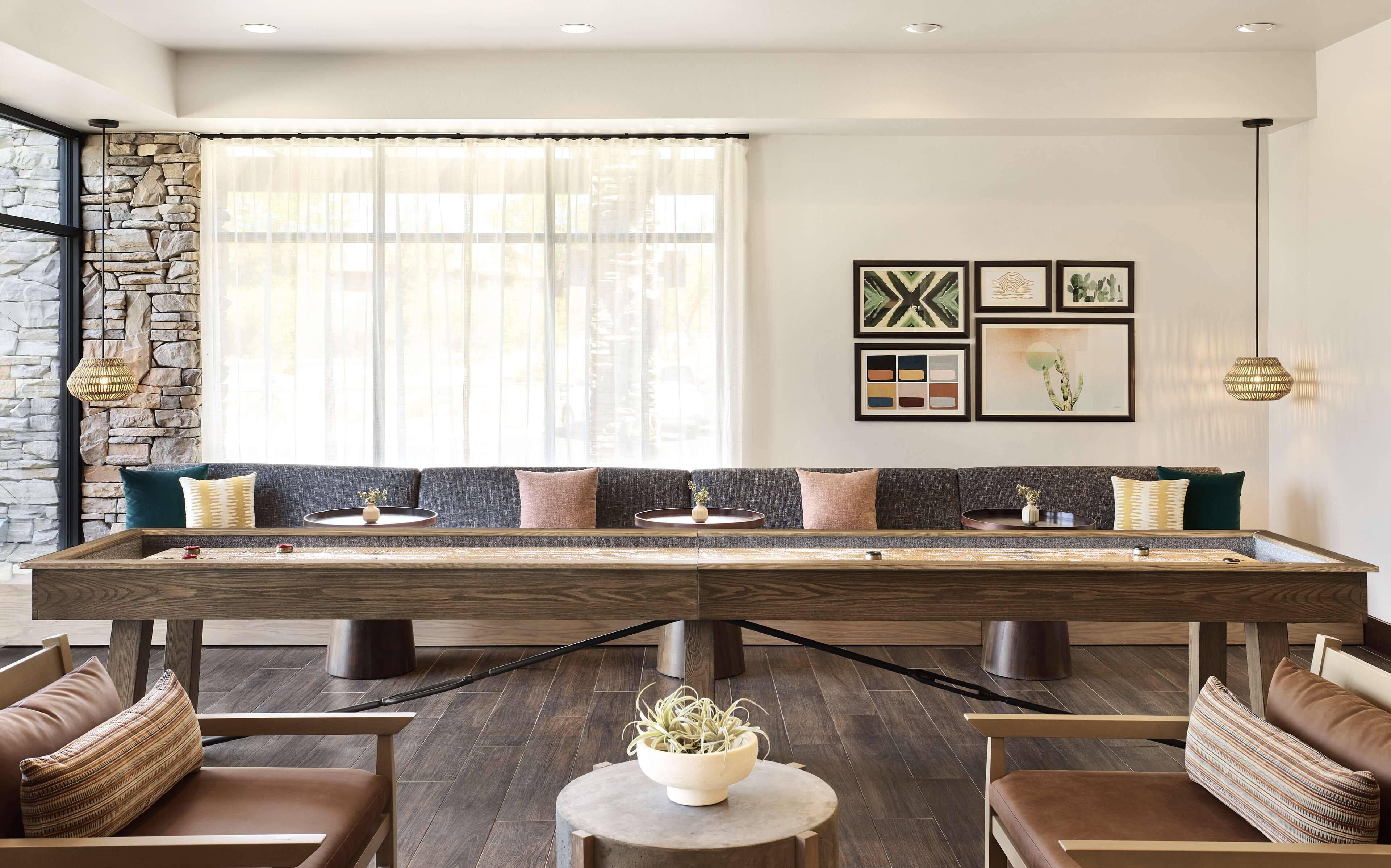 A modern living room with a long wooden table, cushioned seating, and a stone accent wall.