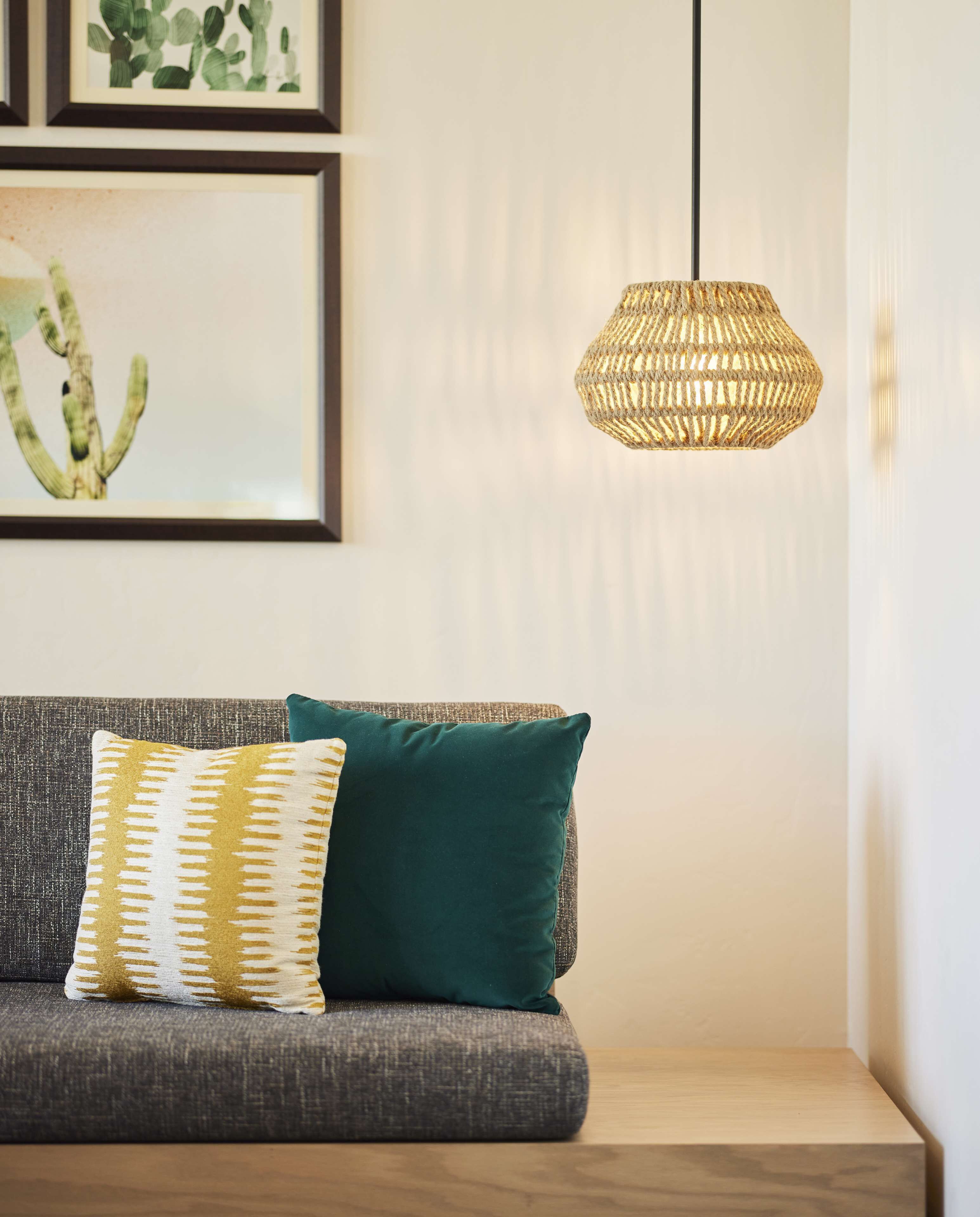 A modern living room with a gray sofa, a green cushion, and a woven pendant light.