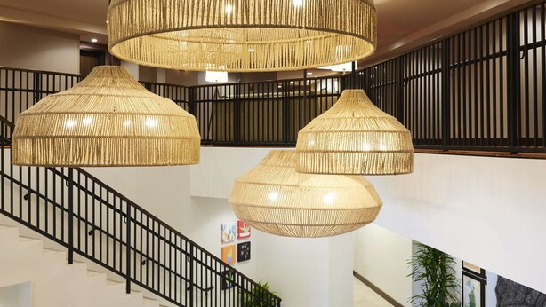 A spacious interior with a staircase, multiple hanging rattan chandeliers, and a modern design aesthetic. - The Eddy Hotel Tucson, Tapestry Collection By Hilton (Tucson)
